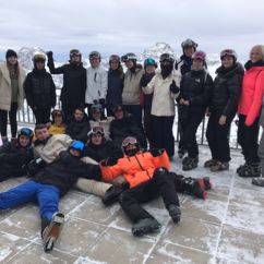 Die Teilnehmer*innen des Skikurses stehen lachend im Schnee vor weißen Bergen